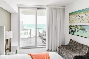 A hotel room with a bed, a sofa, a large window with a view of the ocean, and a painting on the wall. - Beachfront Hyde Getaway (Hollywood)