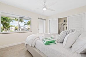A bedroom with a bed, a ceiling fan, a window with a view, and a closet with ironing equipment.
