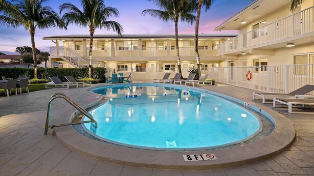 A swimming pool with lounge chairs and palm trees, surrounded by a building with multiple balconies. - Bermuda Isles Villas - King #30 (Lauderdale-by-the-Sea)