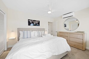 A bedroom with a bed, a dresser, a ceiling fan, an air conditioning unit, and a world map on the wall.
