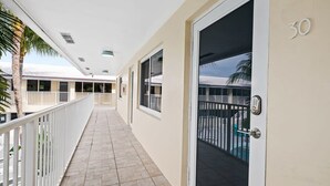 A corridor with a door marked '30', a balcony with a pool, and a palm tree. - Bermuda Isles Villas - King #30 (Lauderdale-by-the-Sea)