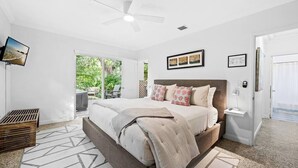 Une chambre avec un lit, un ventilateur de plafond, une télévision et une vue sur la verdure environnante.