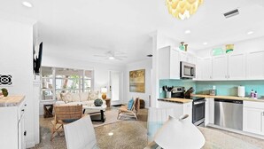 Une cuisine moderne avec des meubles blancs, des appareils en acier inoxydable et un coin repas comprenant une table et des chaises en verre.