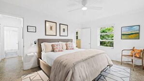 A bedroom with a bed, a ceiling fan, a window with a view, and a door.
