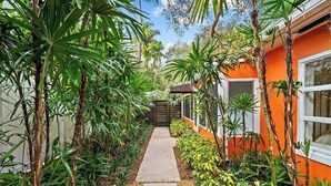 A pathway leading to a building with an orange facade, surrounded by lush greenery.