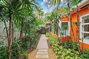 Un chemin menant à un bâtiment à la façade orange, entouré d’une végétation luxuriante.
