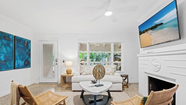 A living room with a sofa, two wicker chairs, a coffee table, a fireplace, a TV, and a large window with a view of greenery.