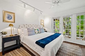 Quarto com cama, mesa de cabeceira, abajur e vista para o verde pela janela.