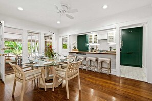 A spacious kitchen with a dining area, featuring wooden flooring, a glass-top table, and a ceiling fan. - Hideaway - Heated Salt Water Pool & Spa (Fort Lauderdale)