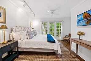 A bedroom with a bed, bedside tables, a ceiling fan, a window with curtains, a painting, and a view of greenery outside. - Hideaway - Heated Salt Water Pool & Spa (Fort Lauderdale)