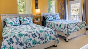 Een hotelkamer met twee bedden, elk voorzien van een bloemenprint beddekleed, een nachtkastje met een lamp en uitzicht op het buiten via een deur.
