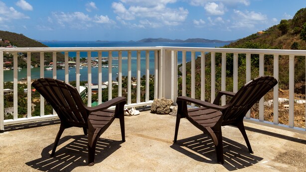 Twee stoelen op een balkon met uitzicht op de kust, boten en een eiland in de verte.