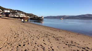 Ein Strand mit Fußabdrücken, einem Steg und Gebäuden im Hintergrund.