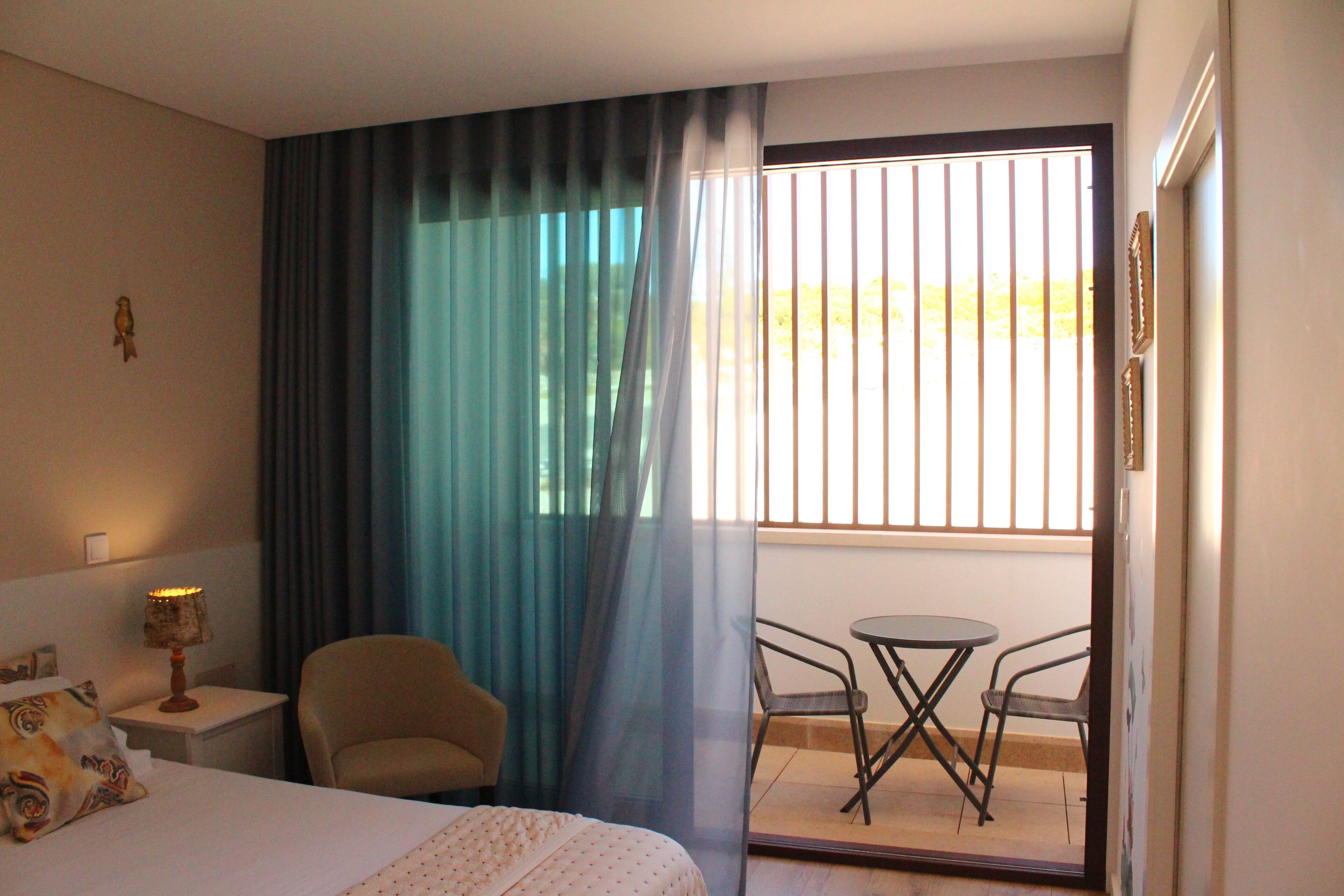 Ein Hotelzimmer mit Bett, Sessel, kleinem Tisch und einem Balkon mit Blick.