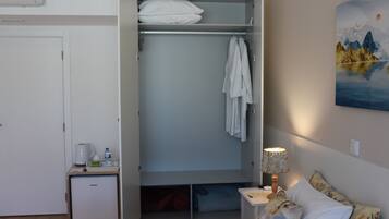 Ein Schlafzimmer mit einem Bett, einem Nachttisch mit Lampe, einem kleinen Nachttisch mit Wasserkocher und Gläsern, einem Kleiderschrank und einem Bild an der Wand.