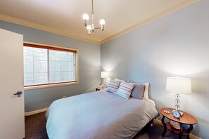Quarto com cama, mesa de cabeceira, abajur, relógio e janela com persianas.