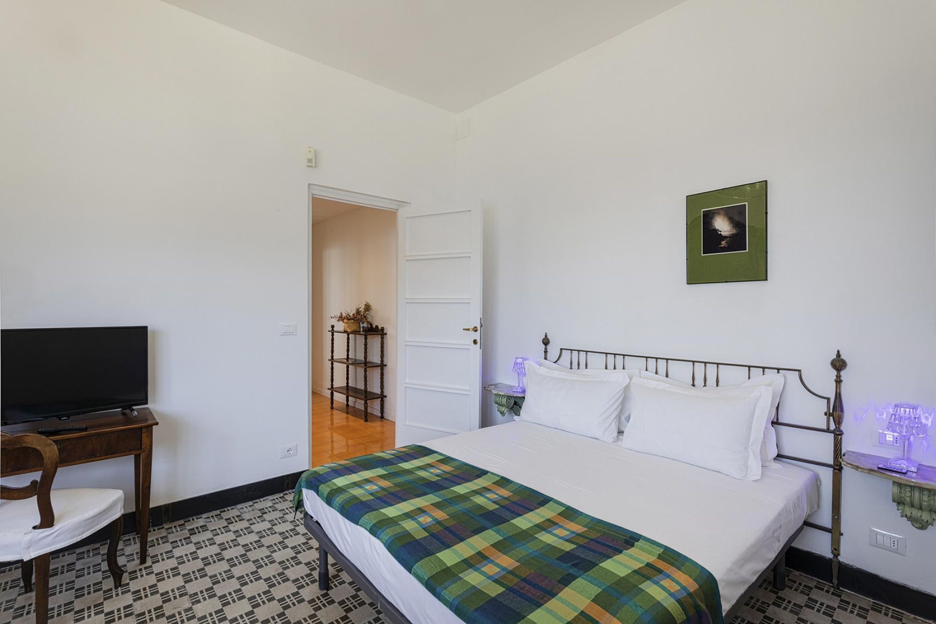 Un dormitorio con cama, televisor, escritorio y puerta que da a otra habitación.