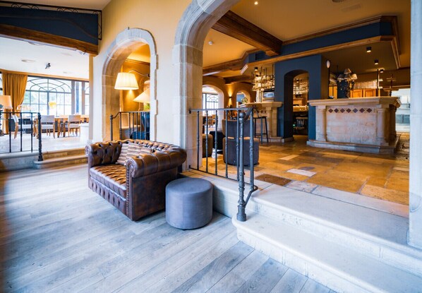 A spacious lobby with a leather sofa, a round ottoman, and a staircase leading to a bar area.