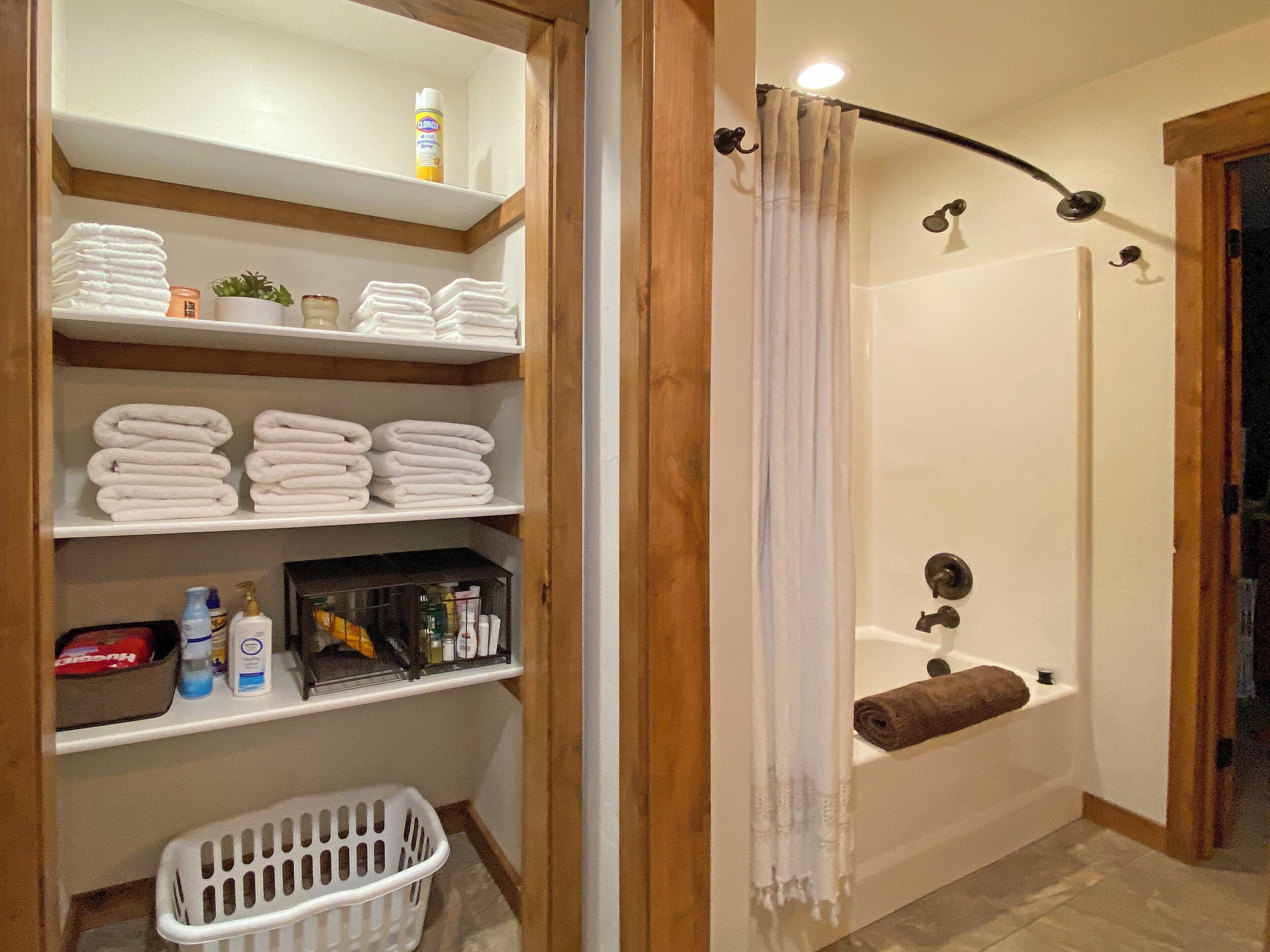 A bathroom with a bathtub, a shower curtain, and shelves with towels and toiletries.