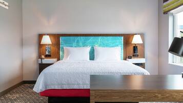 Una habitación de hotel con una cama, lámparas de noche, un escritorio y una ventana.