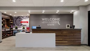 A modern reception area with a wooden reception desk, a sign reading "WELCOME TO THE GOLDEN STATE," and a wall with a circular design. - Hampton Inn Concord (Concord)