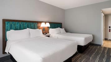Une chambre d’hôtel avec deux lits, une tête de lit en bois, une table de chevet avec des lampes et un sol recouvert de moquette.