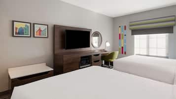 Une chambre d’hôtel avec deux lits, une télévision, un bureau avec une chaise, un miroir et des œuvres d’art accrochées au mur.
