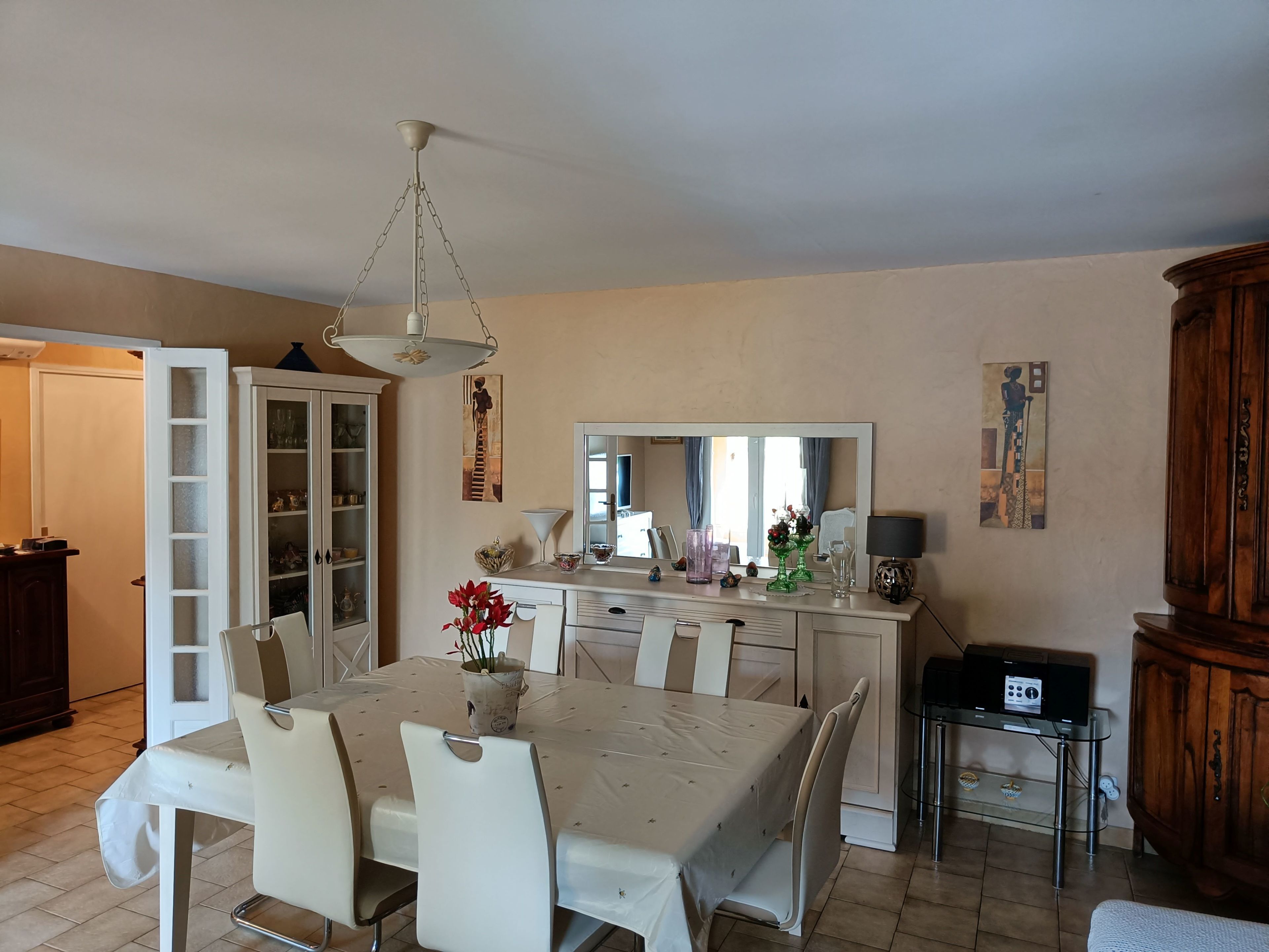 A dining area with a table set for four, a cabinet with glass doors, a mirror, and a wooden cabinet.