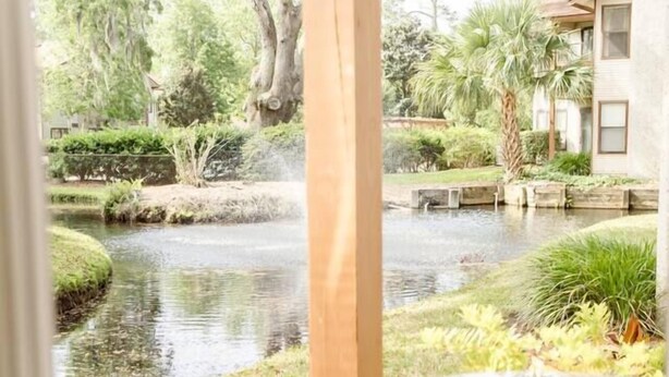 Een terras buiten met twee metalen stoelen en een tafel, met uitzicht op een vijver en weelderige begroeiing.
