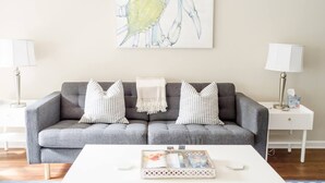 Een woonkamer met een grijze bank, gestreepte kussens, een witte salontafel en een abstract schilderij in een lijst aan de muur.