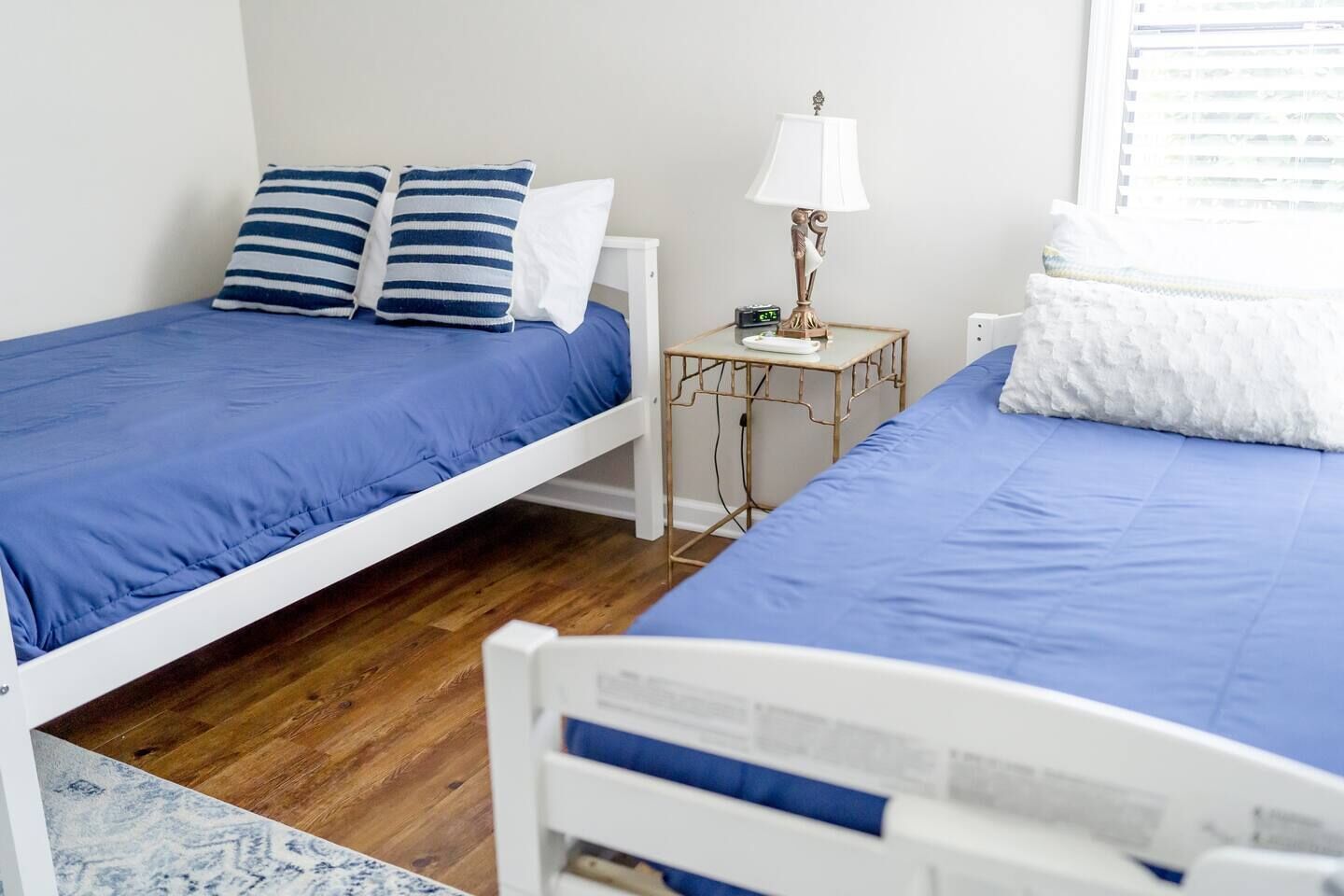 Une chambre avec deux lits simples, une table de chevet avec une lampe et une petite table avec une horloge.