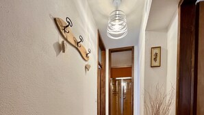 Un couloir doté d’un plancher en bois, d’un luminaire fixé au mur, d’un élément décoratif mural et d’un vase contenant des branches.