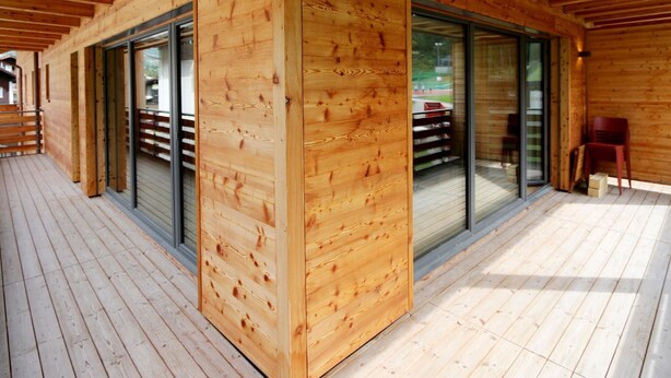 Una cabaña de madera con terraza, puertas correderas de vidrio y una silla roja.