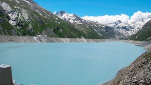 Un paisaje de montaña con un lago azul cristalino, terreno rocoso y picos nevados.