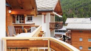 Eine Holzhütte mit Balkon, einem Essbereich und Blick auf einen bewaldeten Gebirgszug.