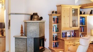 Ein gemütliches Wohnzimmer mit Kamin aus Stein, Holzregalen, einem weißen Sessel und einem Glastisch.