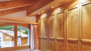 Ein Schlafzimmer mit einem großen Bett, einem Holzschrank und einem Fenster mit Blick auf Häuser.