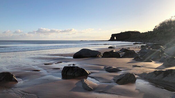 A beach with large rocks and a clear sky.