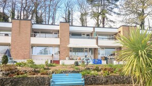 A multi-story building with a stone retaining wall, a blue bench, and a variety of plants.