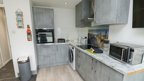 A modern kitchen with grey cabinets, a built-in oven, a microwave, and a sink.