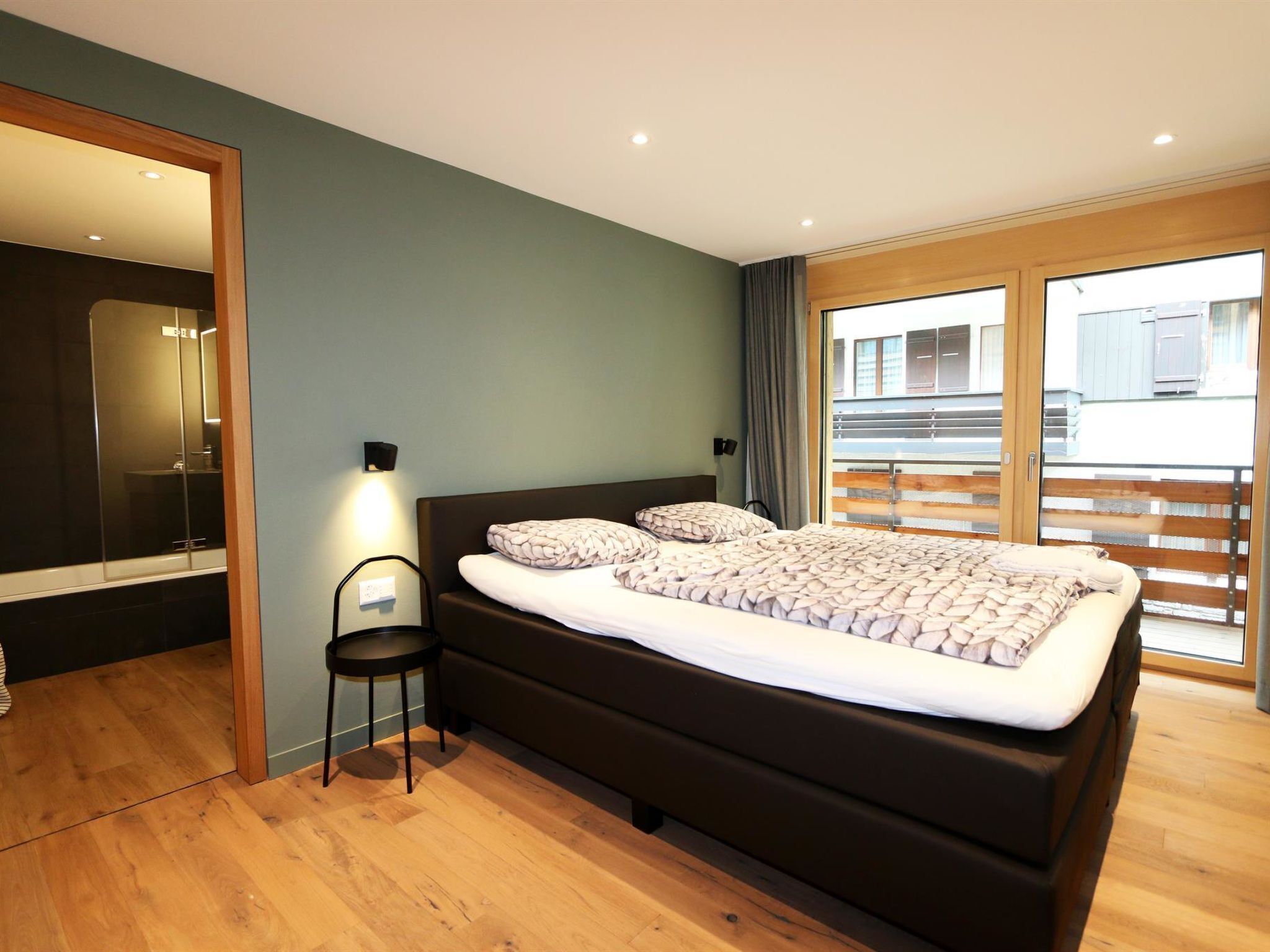 Una camera da letto moderna con un letto grande, una poltroncina, uno specchio e vista sul balcone esterno.