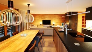 Een moderne keuken met een houten kookeiland, een eethoek met een houten tafel en stoelen, en hanglampen.