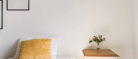 A neatly arranged bedroom with a bed, a bedside table with a vase of flowers, and a framed inspirational quote on the wall.