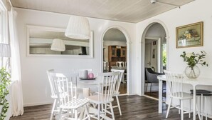 A dining area with white chairs and a table, a hanging light fixture, and a mirror above the table.