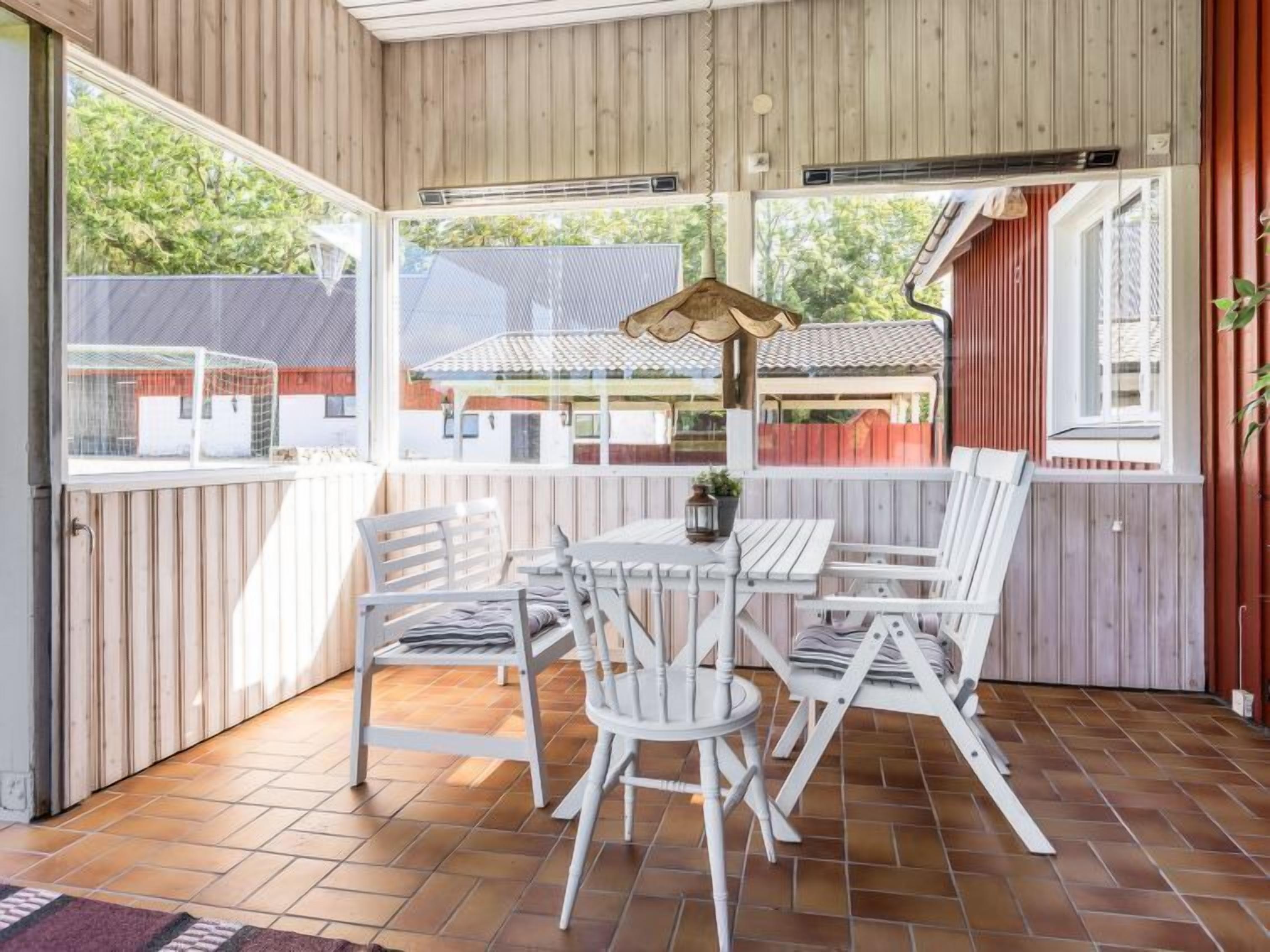 A covered patio with a wooden table and chairs, a lantern, and a view of neighboring houses.