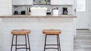 A kitchen with white cabinetry, a stainless steel microwave, a coffee maker, and two wooden stools. - Charming Home Near Midtown (Houston)