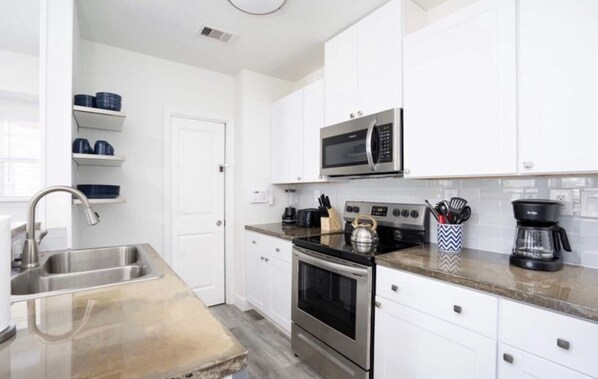 Modern kitchen with microwave, oven, and sink, featuring a spacious counter with a kettle, coffee maker, and utensils.