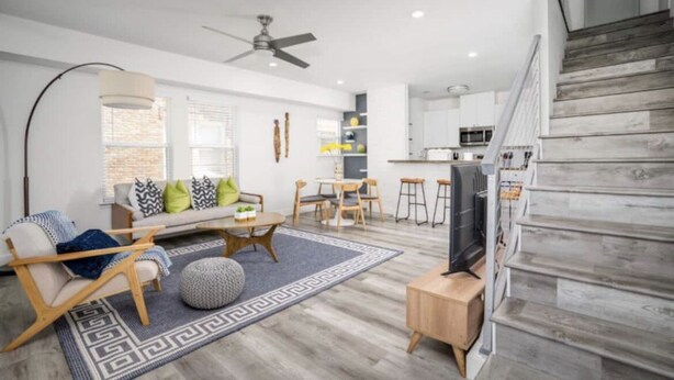 A modern living room with a sofa, coffee table, and TV, a staircase, and a kitchen in the background. - Charming Home Near Midtown (Houston)