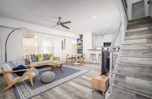Relax in a spacious living area with a sofa, chair, and TV, plus a kitchen with white cabinets and a bar stool.