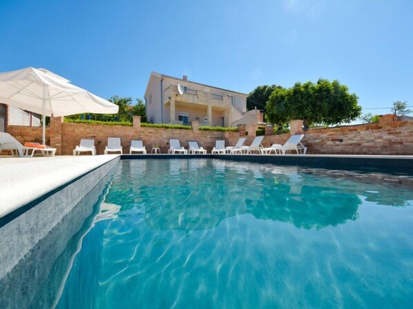 A swimming pool with white lounge chairs and a white umbrella.
